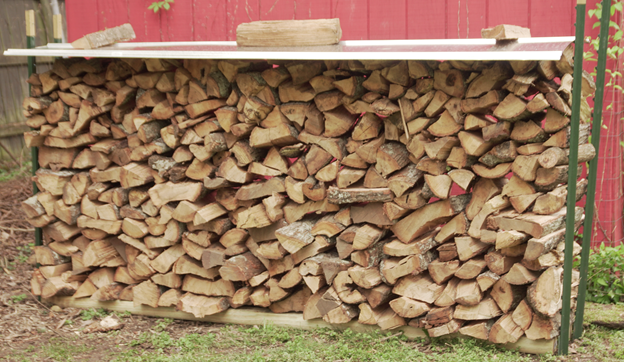 A neatly stacked pile of firewood in front of a red shed.