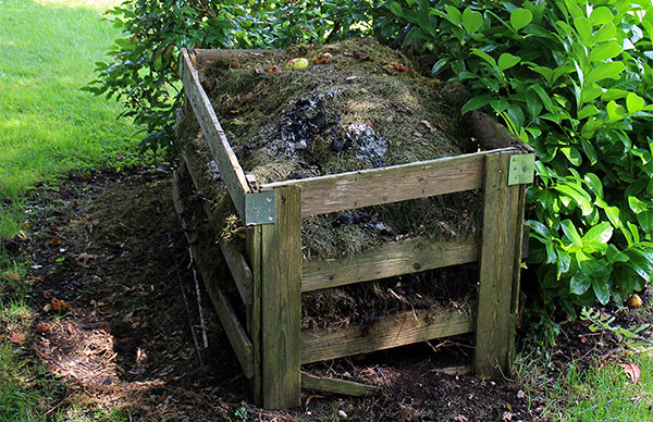A wooden compost bin filled with organic waste in a garden setting.