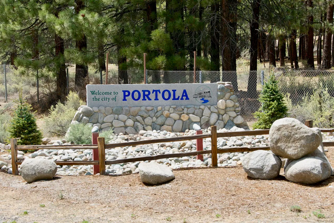 City welcome sign for "PORTOLA" with landscape, rocks and trees.