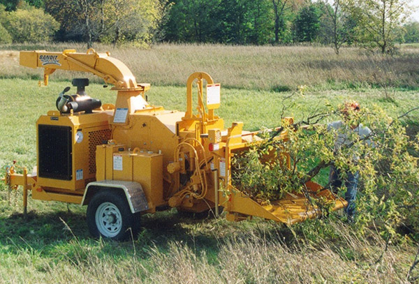 A wood chipper machine processing branches in a field.