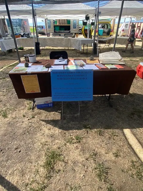 An information booth with a table, pamphlets, and a sign about air quality and wildfire under a canopy tent.