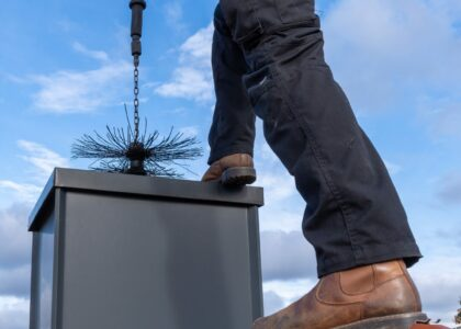 A person is cleaning a chimney with a brush against a blue sky.