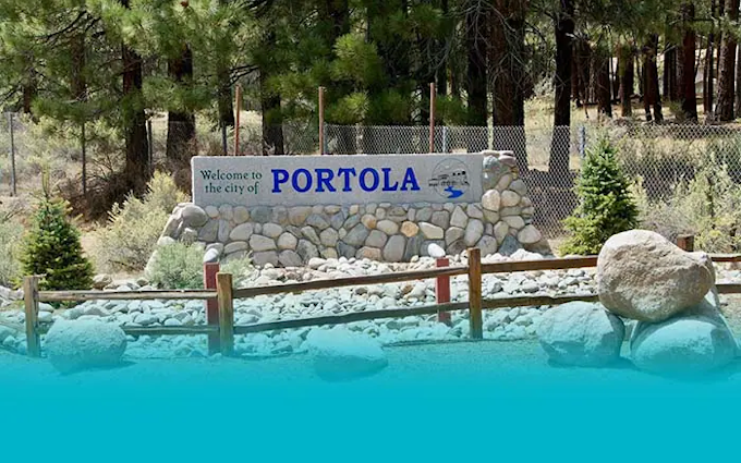 A welcome sign to the city of Portola surrounded by rocks, trees, and a fence.