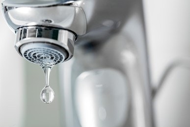 A close-up of a chrome faucet with a single droplet of water about to fall.