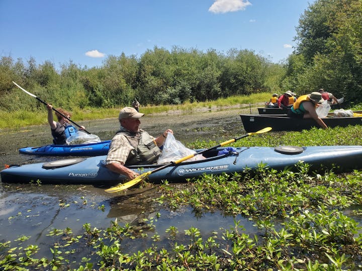 May contain: plant, vegetation, face, head, person, photography, portrait, clothing, hat, water, vest, adult, male, man, lifejacket, oars, outdoors, tree, nature, wilderness, grass, boat, transportation, vehicle, land, canoe, kayak, rowboat, helmet, accessories, bag, and handbag