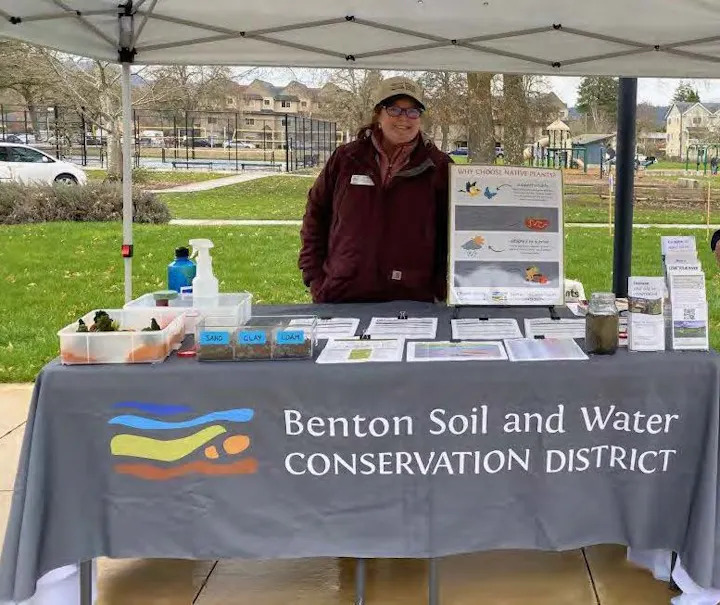 A person stands at a table promoting the Benton Soil and Water Conservation District and information about native plants.