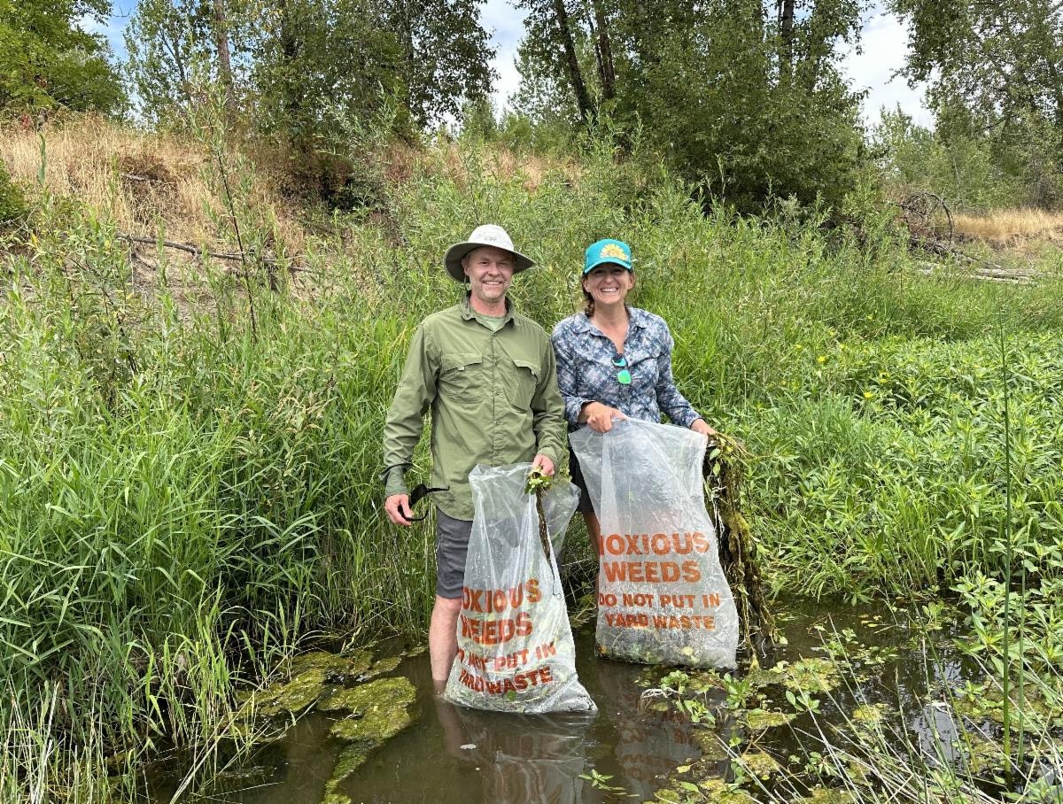 Michael Ahr (BSWCD) and Vanessa Youngblood (Willamette Riverkeeper) holding bags of aquatic invasive plants during 2024 paddle and pull event.