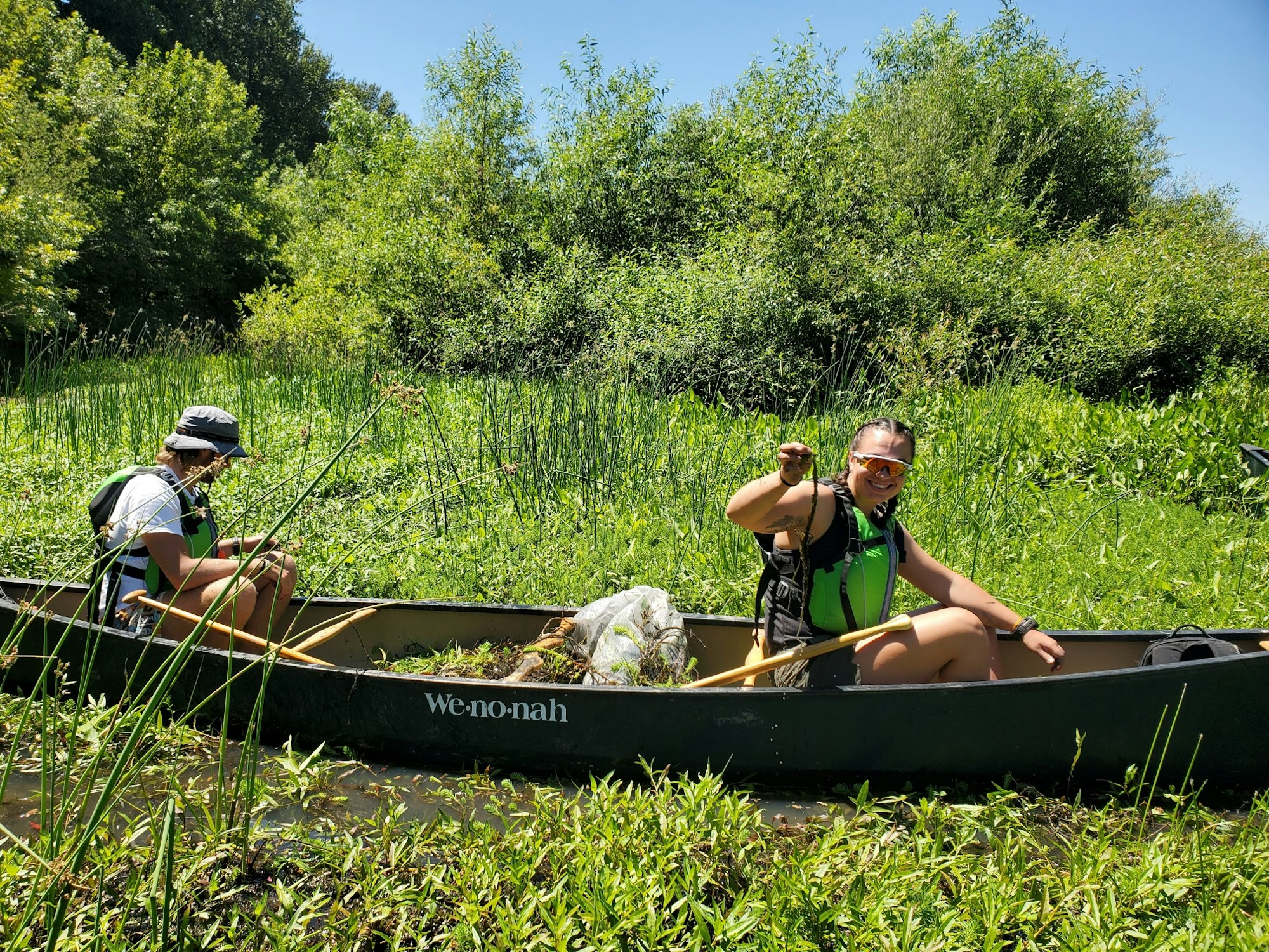 May contain: boat, canoe, canoeing, leisure activities, person, rowboat, sport, transportation, vehicle, water, water sports, accessories, bag, handbag, clothing, hat, glasses, plant, and vegetation