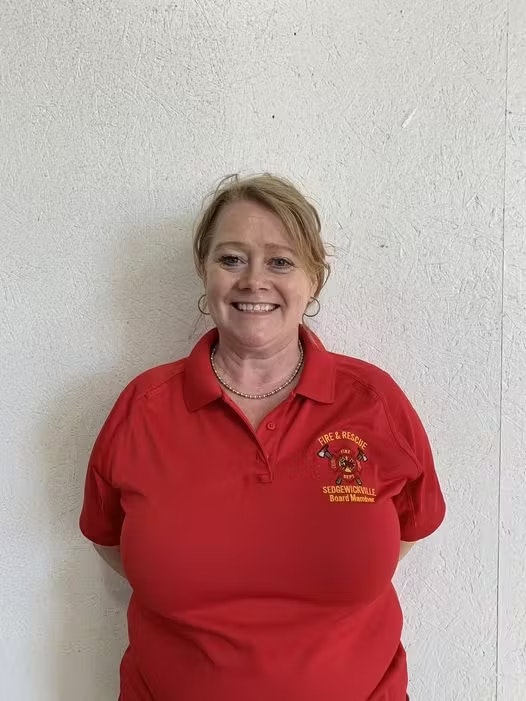 A person wearing a red polo shirt with "Sedgwickville Fire & Rescue" logo, smiling against a plain wall.