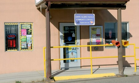 A colorful entrance of the Santa Clara Pueblo Community Library with a sign, open flag, mailboxes, and bright windows.