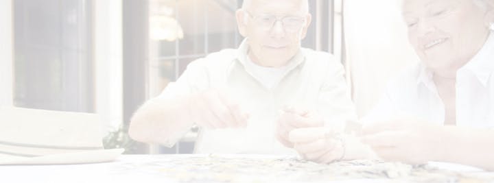 Two people are doing a puzzle together at a table indoors, with a hat placed nearby.