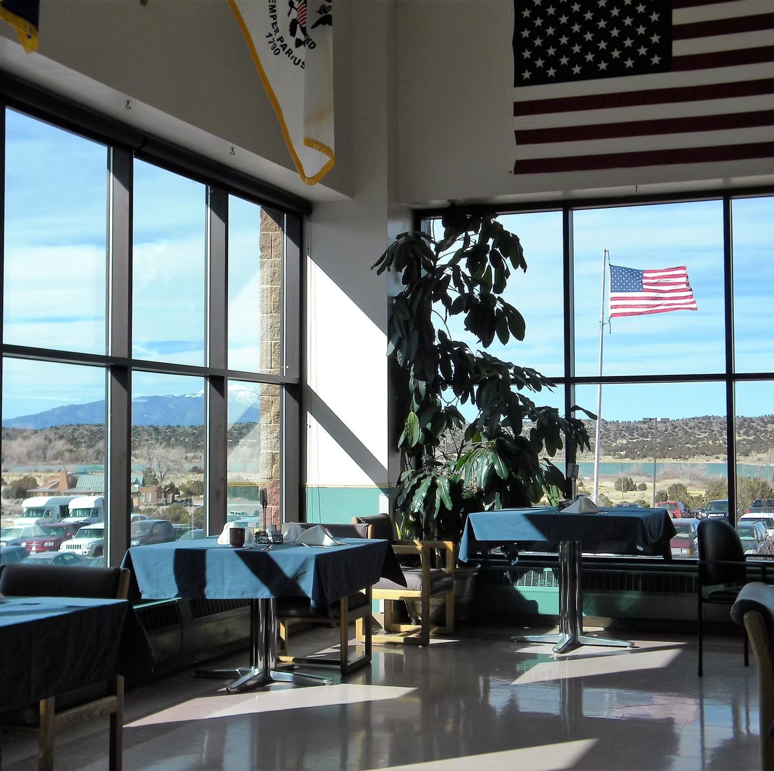 A bright room with tables, chairs, large windows, and American flags, with a scenic view outside.