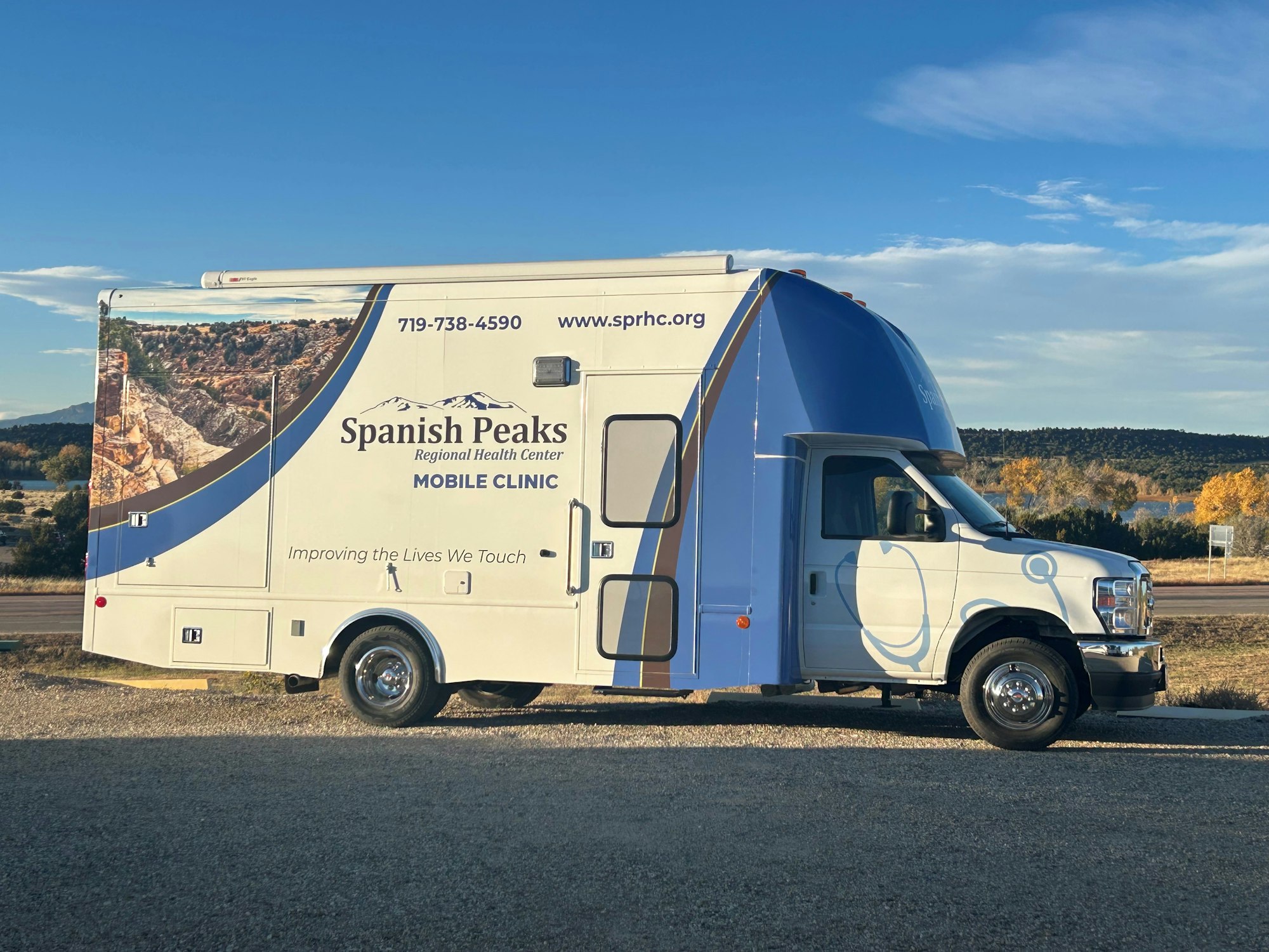 Mobile medical clinic van labeled "Spanish Peaks Regional Health Center" with contact details, parked outdoors.