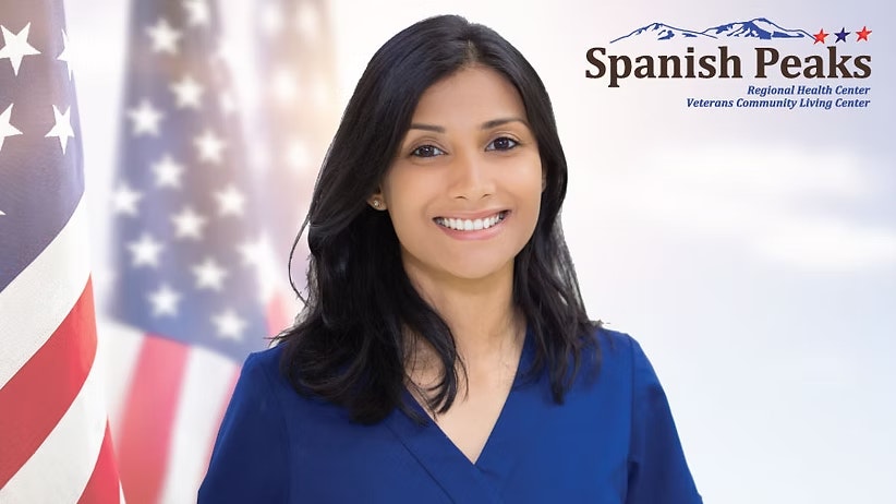 Smiling person in blue outfit with American flags and Spanish Peaks logo in the background.