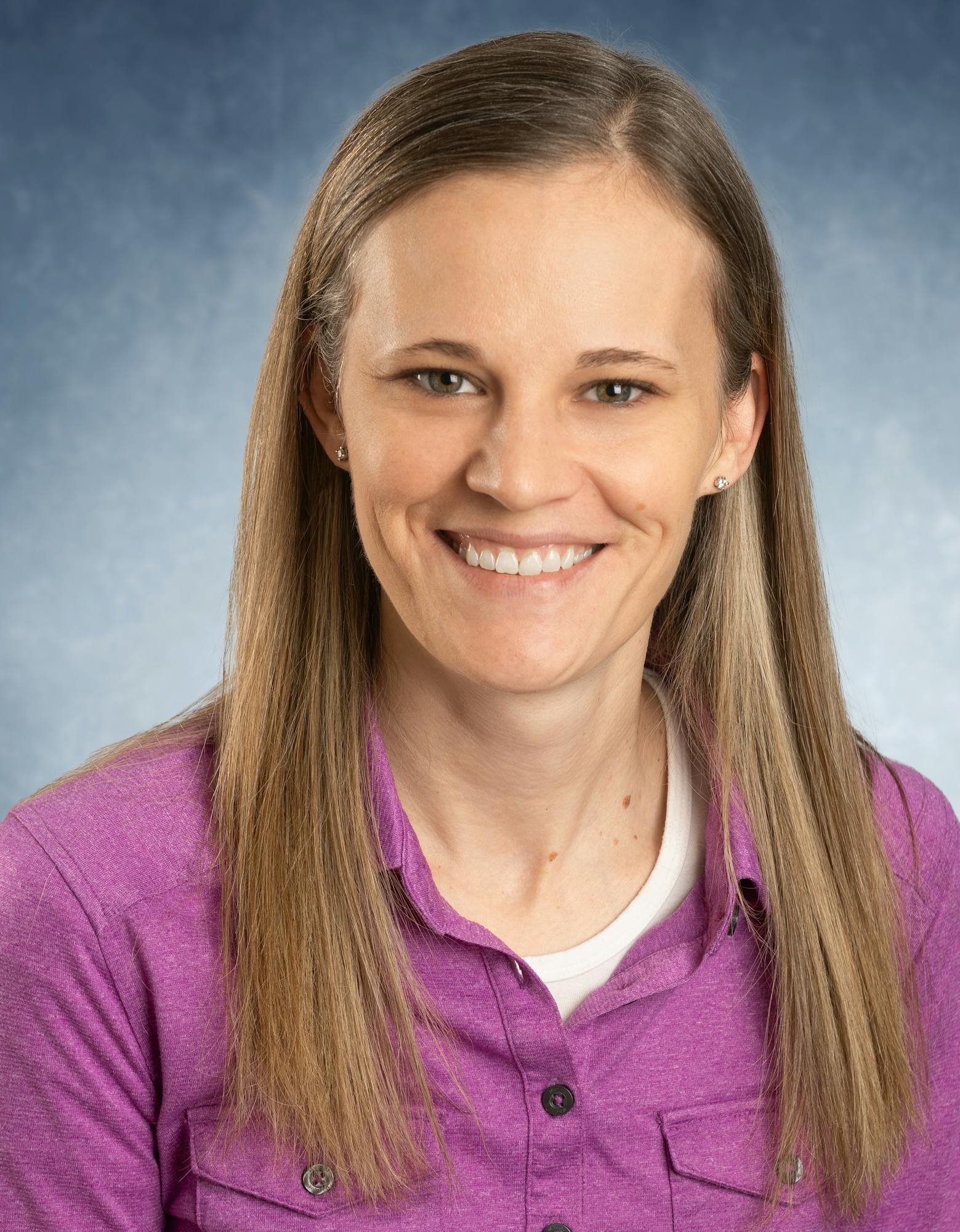 A person wearing a purple shirt, smiling at the camera against a blue background.