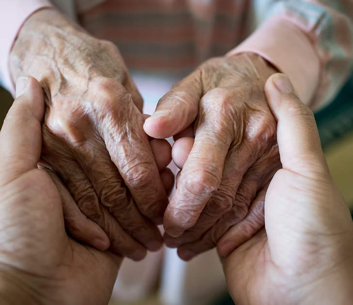 Two hands supportively holding another's aged hands, conveying care and support.