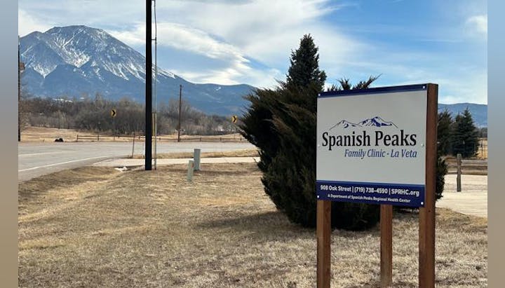 A road sign for "Spanish Peaks Family Clinic-La Veta" with a mountain in the background.