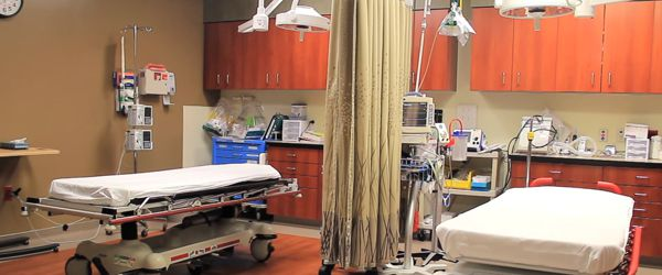 A hospital room with two empty beds, medical equipment, curtains, cabinets, and various medical supplies.