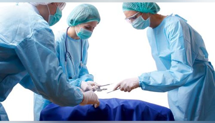 Three surgeons in blue scrubs and masks working together over an operating table.