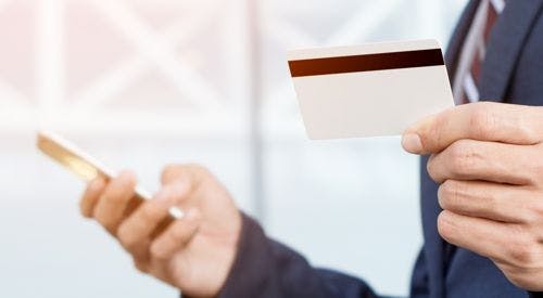 A person in a suit is holding a credit card and a smartphone, possibly making a transaction.