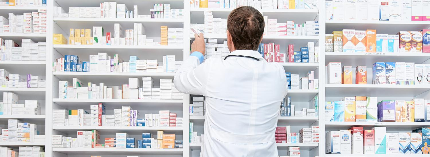 A pharmacist in a white coat organizes medicine boxes on shelves.