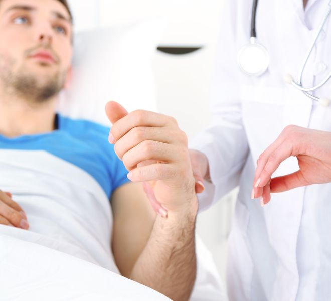 A doctor checks a patient's pulse in a hospital bed.