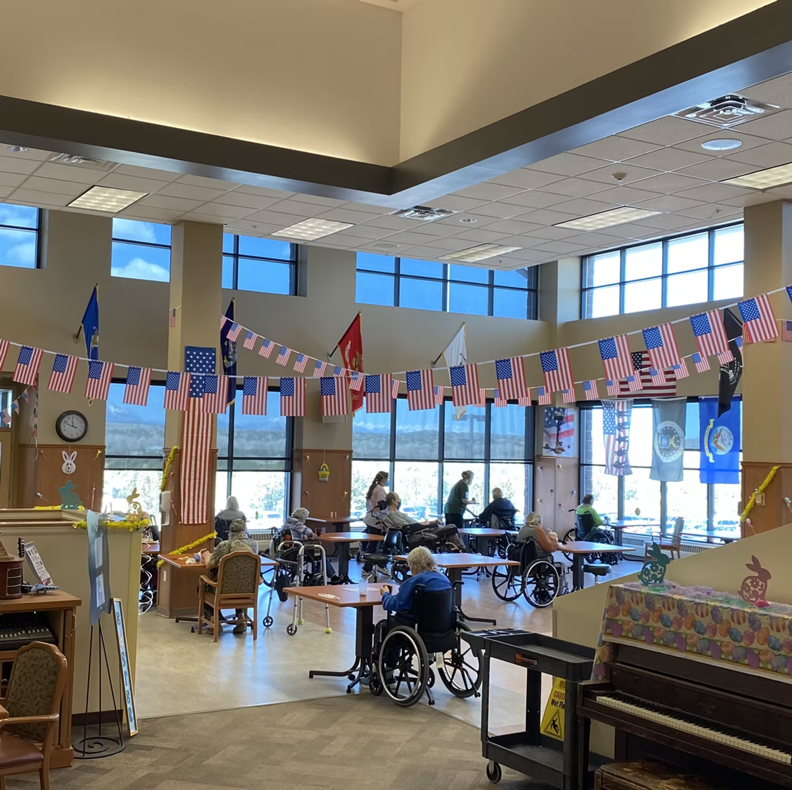 Large room with American flags, people in wheelchairs, and staff assisting; possibly a care or community center.