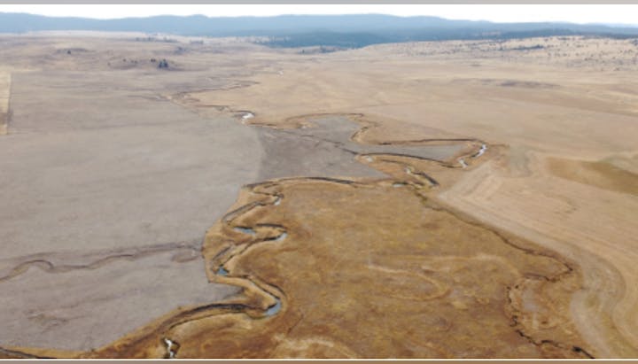 An aerial view of a dry, barren landscape featuring winding streams, open fields, and distant mountains.