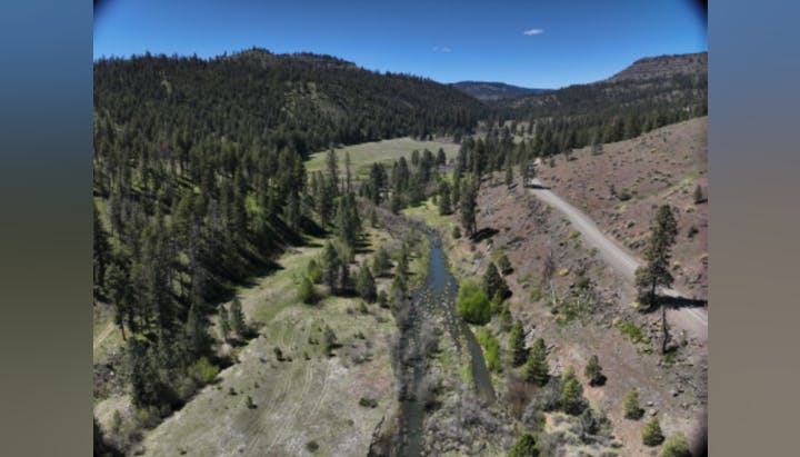 Aerial view of a serene landscape featuring a river, lush greenery, and rolling hills under clear blue skies.