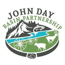 The image is a logo for the John Day Basin Partnership, featuring mountains, wildlife, and a river.