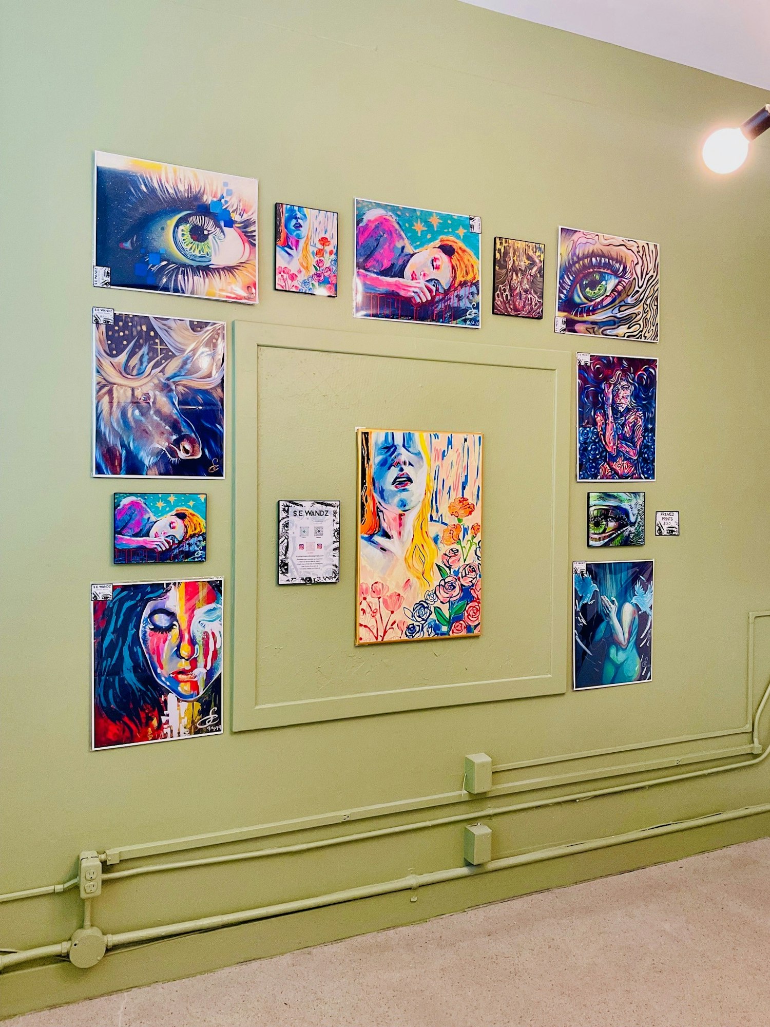 A vibrant gallery wall features various colorful artworks, including portraits and an eye, against a green backdrop.