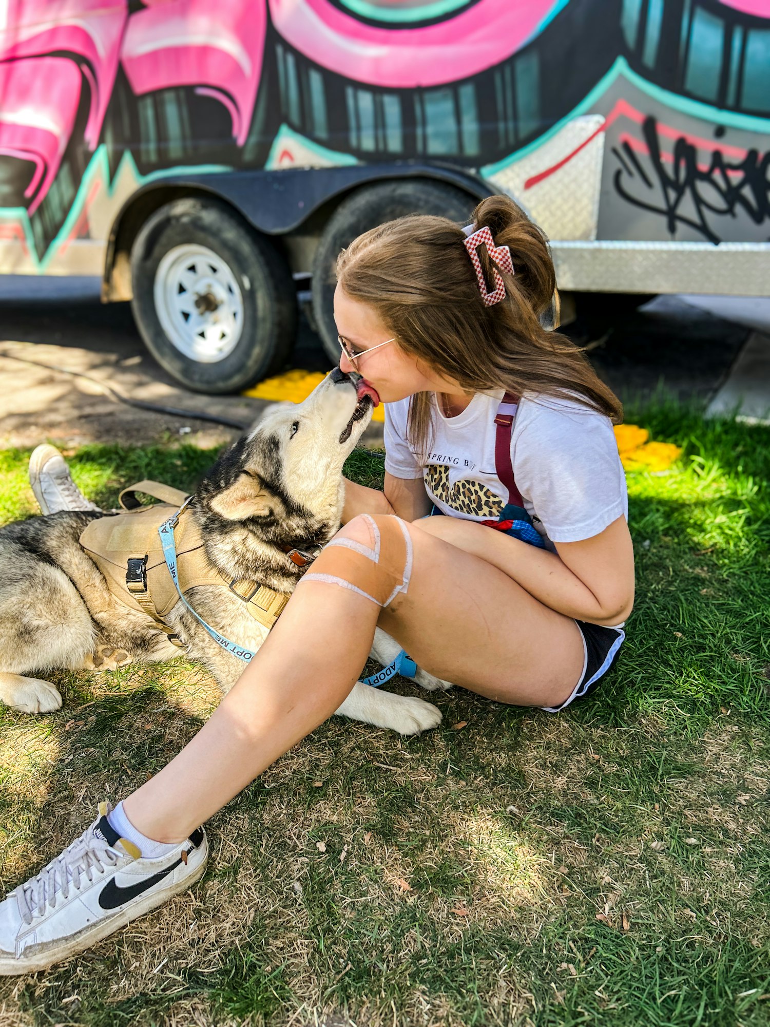 A woman is affectionately interacting with a dog near a vehicle with graffiti art.