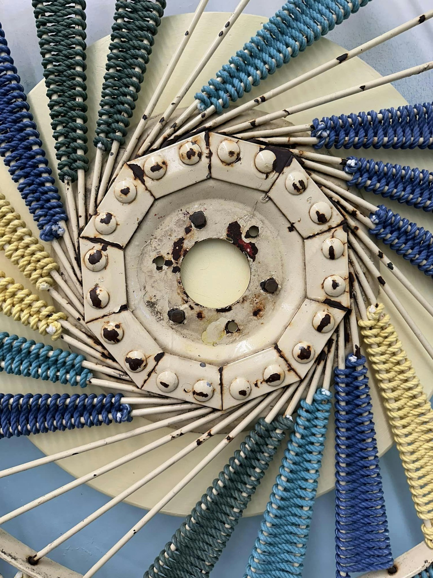 Colorful strings tightly wrapped around spokes radiating from a rusty center hub.