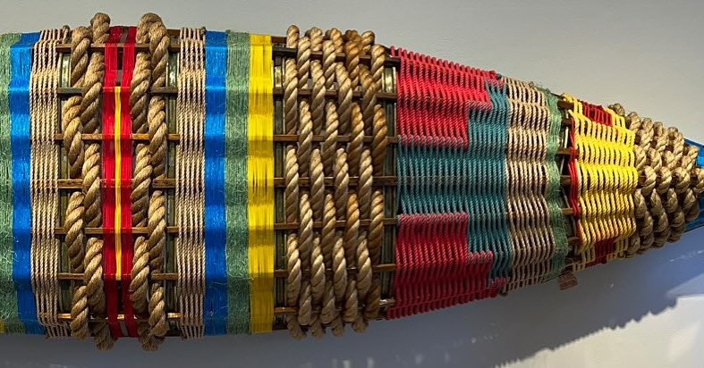 Colorful woven tapestry with intricate patterns wrapped around a cylinder, displayed against a white background.