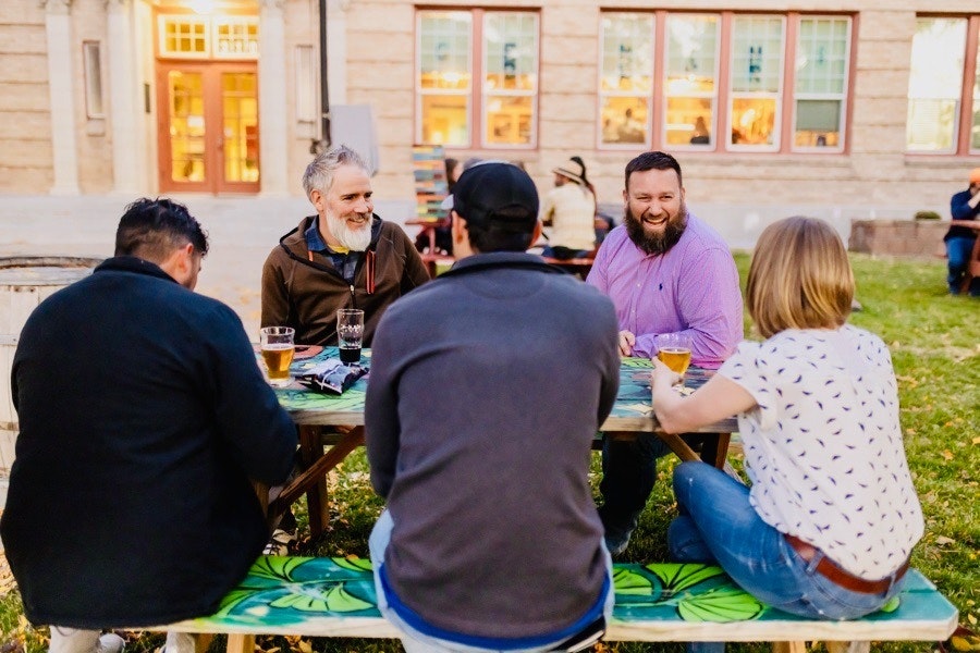 A group of people sitting around a table, enjoying drinks and engaging in conversation outdoors.