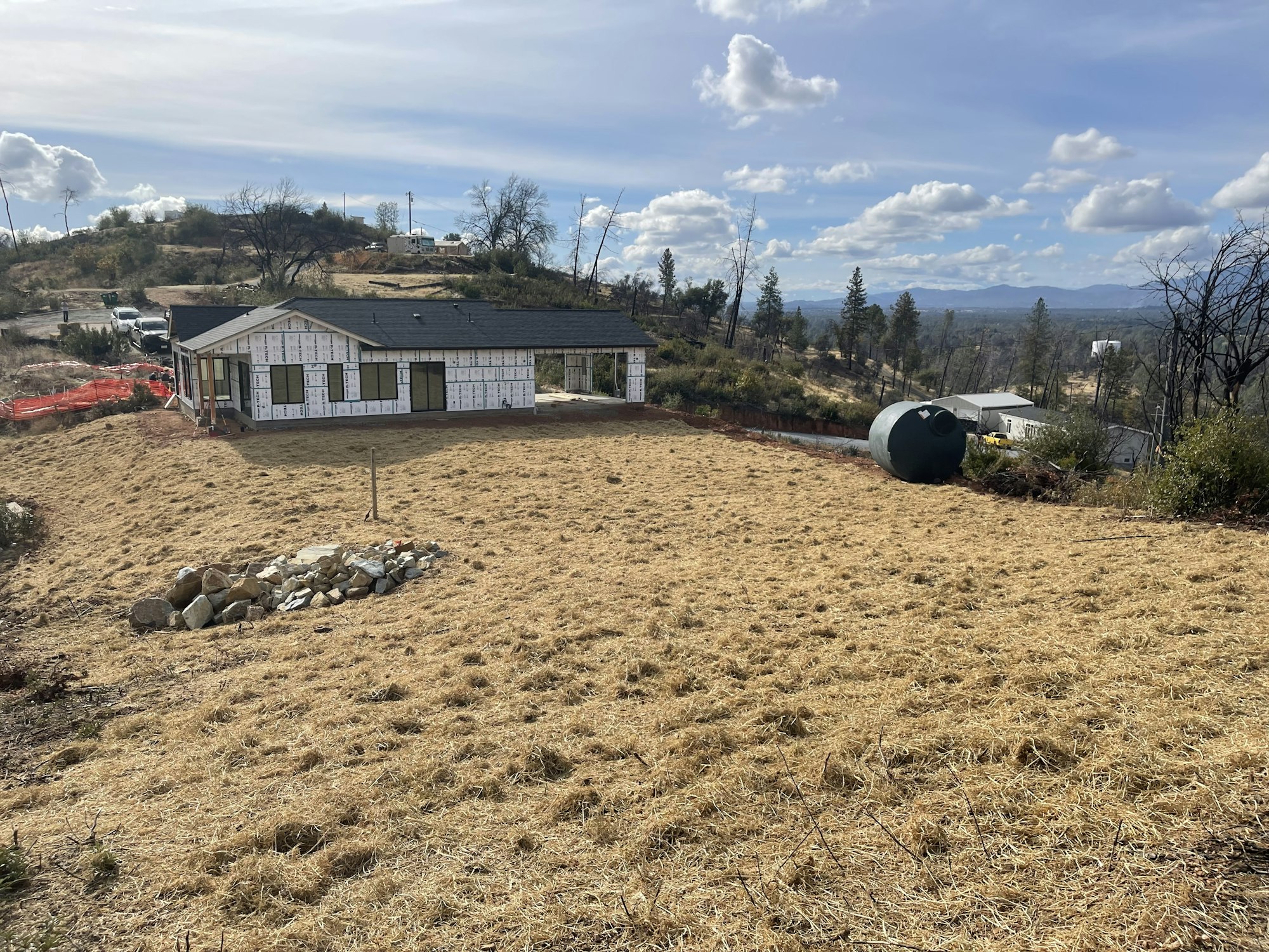 A house under construction on a grassy hill with a water tank in a rural landscape.