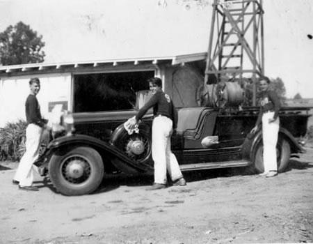 Vintage photo: Three individuals beside an old firetruck, possibly firefighters.