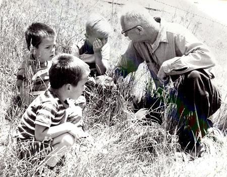 An elderly man and three children in a field, possibly engaged in a conversation or activity.