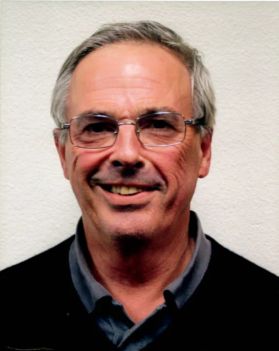 A smiling man with glasses against a pale background.