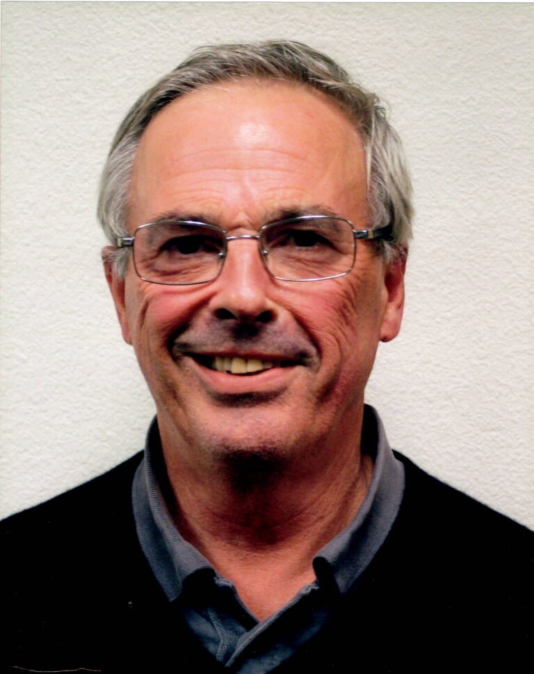 A smiling man with glasses against a pale background.