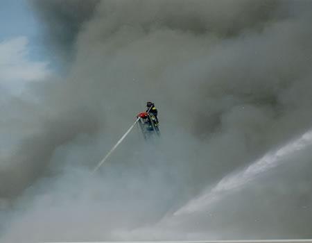 A firefighter using a hose amidst thick smoke.