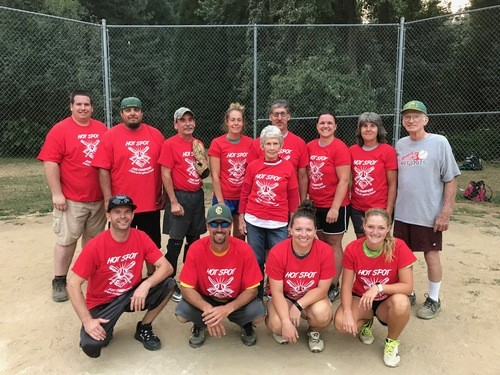 A softball team wearing matching red shirts poses on a dirt field.