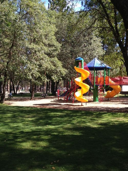 Playground in a park with a spiral slide, surrounded by trees and grass.