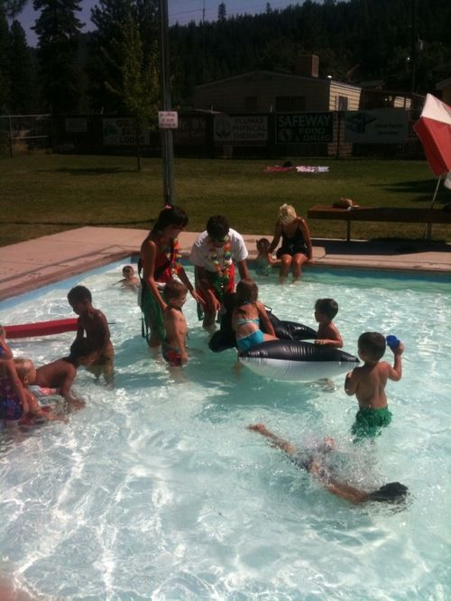 Kids playing in a small outdoor pool with inflatable toys, while adults supervise.
