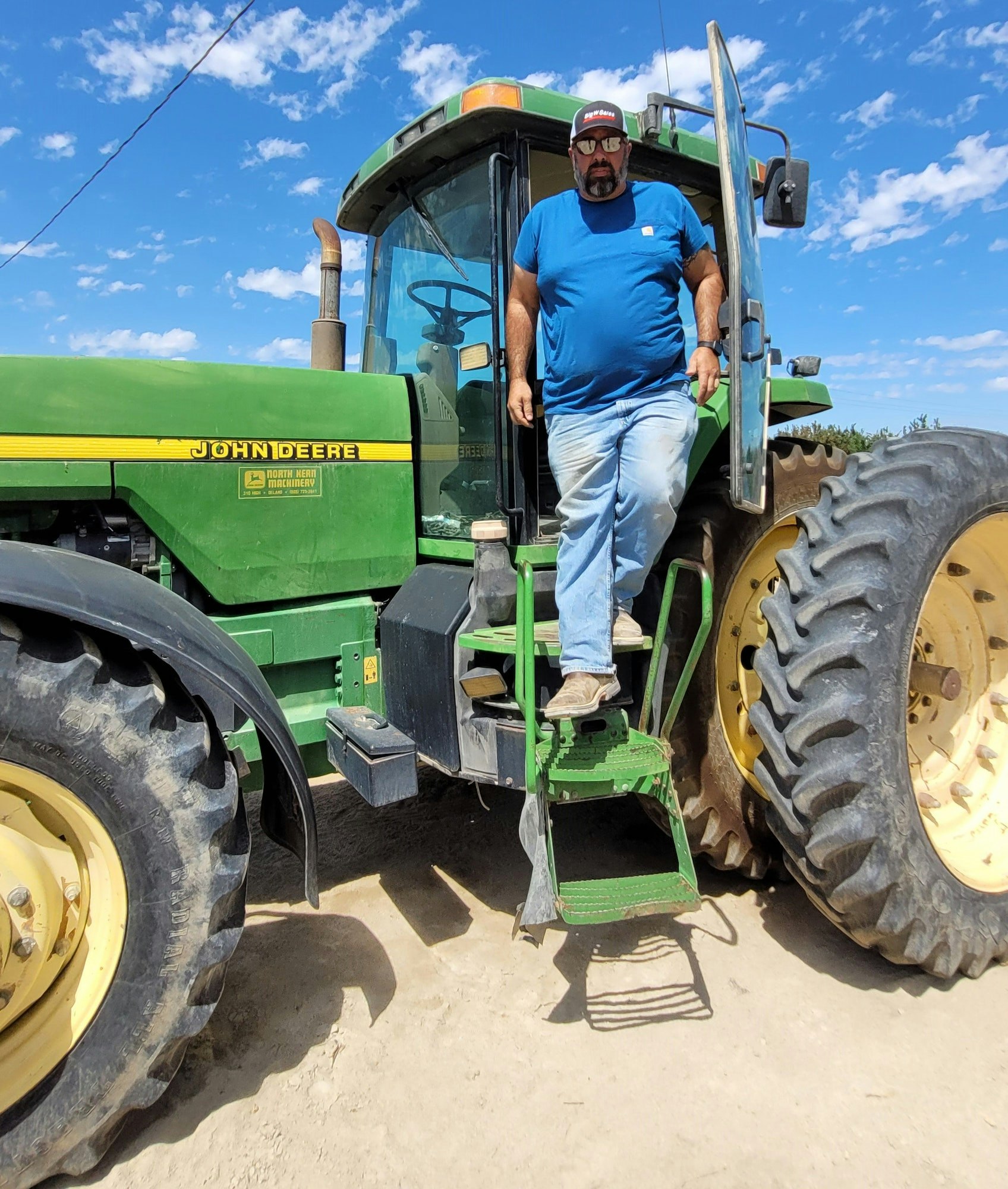 May contain: adult, male, man, person, clothing, footwear, shoe, accessories, glasses, machine, wheel, wristwatch, tractor, transportation, vehicle, pants, hat, and outdoors