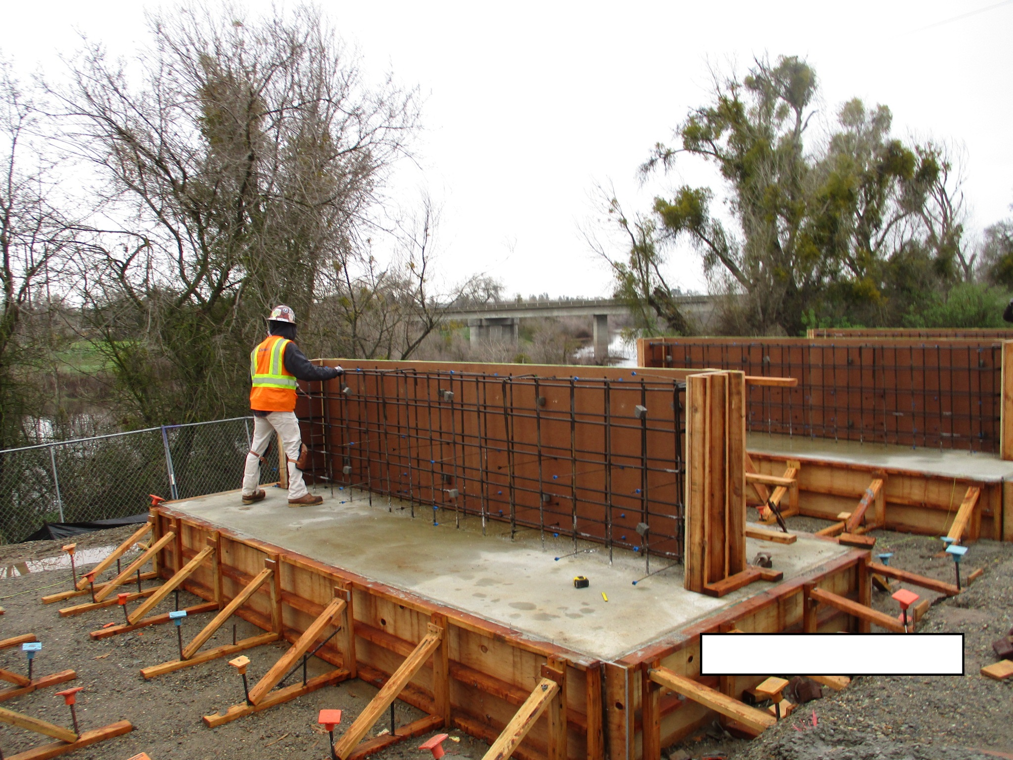 Construction site with a worker setting up concrete forms near a river.