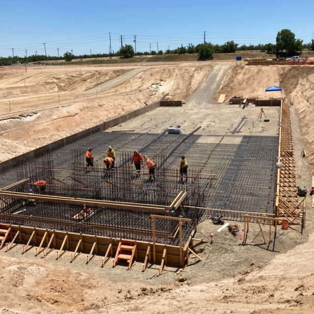 Construction workers on a site with rebar framework for concrete, indicating early stages of a large structure.