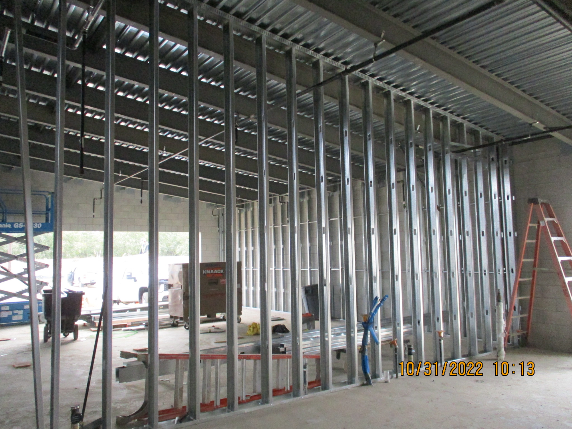 Interior construction site with metal stud framing, a ladder, and building materials.