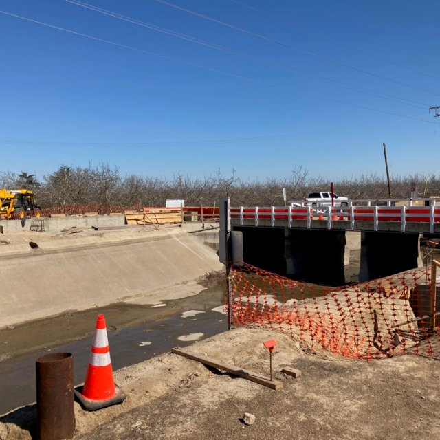A construction site with a barrier, orange safety cone, safety netting, and a clear sky.