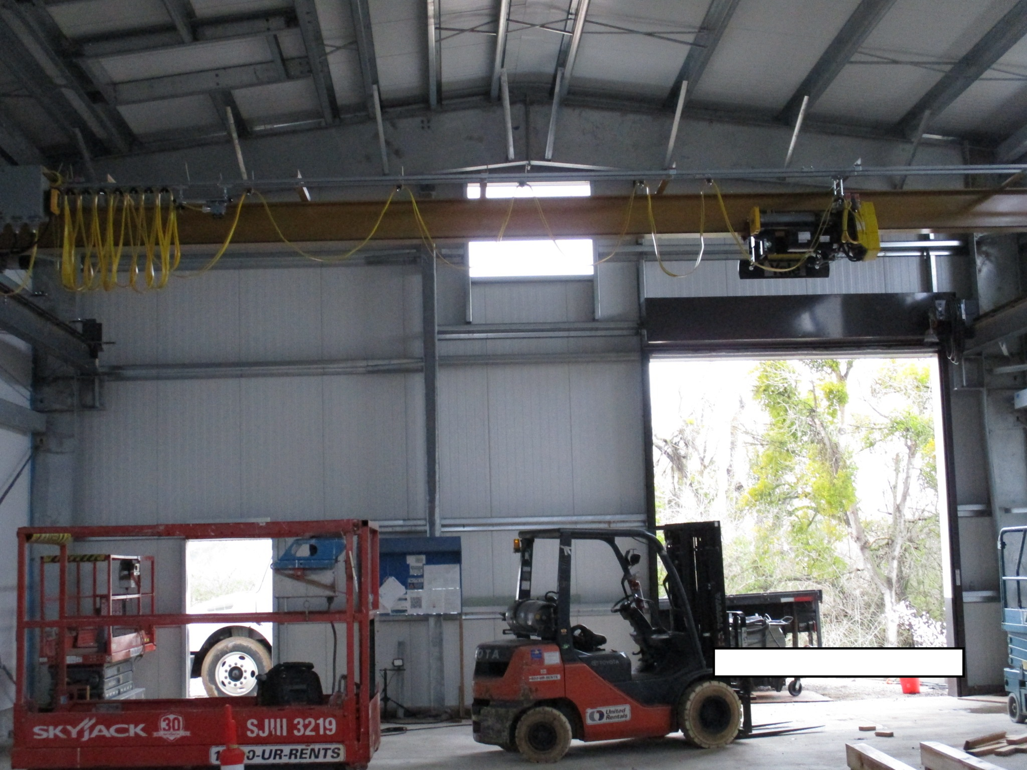 Industrial workshop with a forklift, scissor lift, and overhead crane.